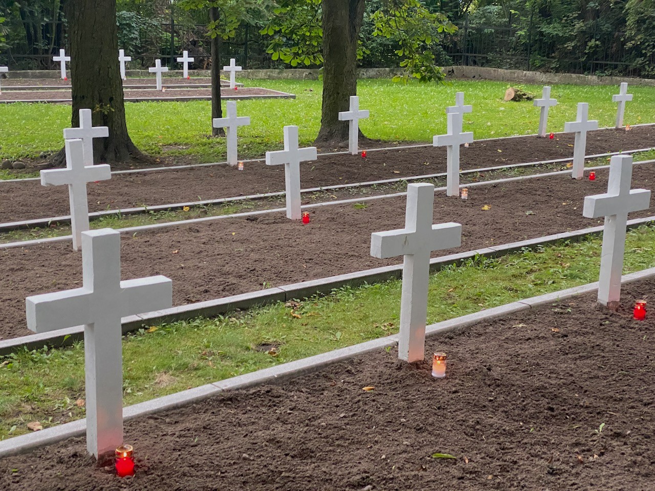 Cmentarz z białymi krzyżami bez oznaczeń. Pod każdym krzyżem stoi pojedynczy zapalony znicz