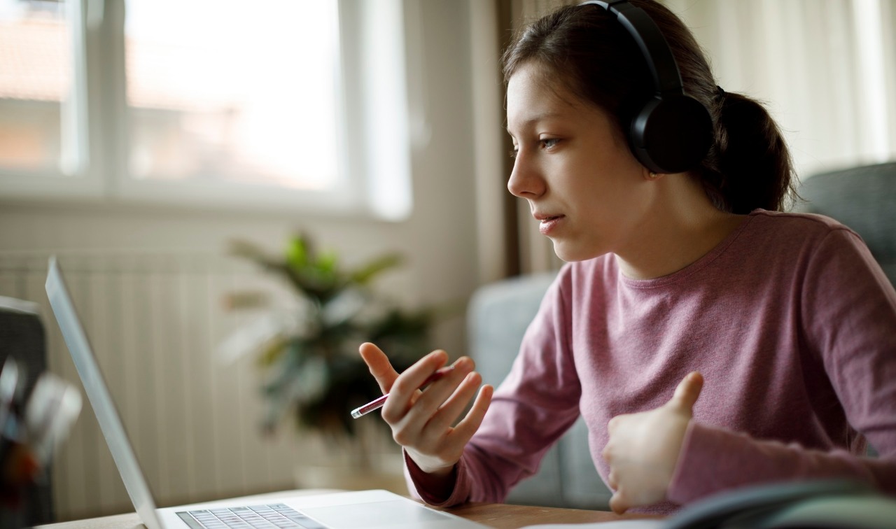 Teenage girl with headphones having online school class at home